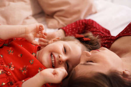Mom and her little daughter lie on the bed facing each other. They are happyの写真素材