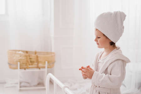 Smiling little girl in a white bathrobe after a bath. White cozy interior.の写真素材