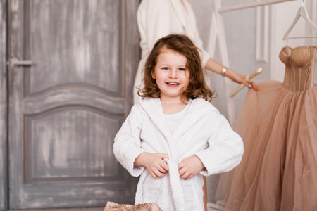 Smiling little girl in a white bathrobe after a bath. White cozy interior.