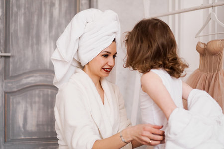 Attractive mother in a white bathrobe is dressing her little daughter.の写真素材