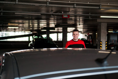 A young man in a tracksuit stands next to a car in an underground parking lot