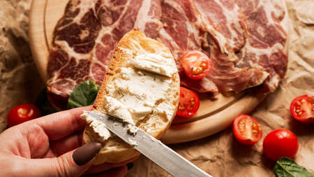 A womans hand holds a bruschetta and spreads curd cheese with a knifeの写真素材