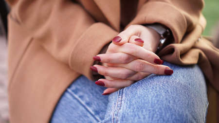 Female hands with red manicure folded on the knee. The concept of waiting in line. Emotion of calmness, depression. Gesture during a serious conversation or communication with a psychologistの写真素材