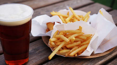 Dark beer and fries on a wooden table. Food court. Takeaway food, food festival. Unhealthy food conceptの写真素材