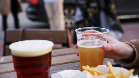Girlfriends drink beer at the street food festival. Plastic glass of beer in hand. French fries, unhealthy foodの写真素材