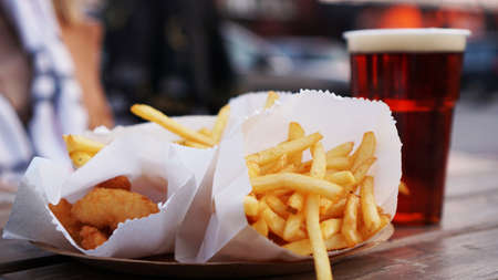 Dark beer and fries on a wooden table. Food court. Takeaway food, food festival. Unhealthy food conceptの写真素材