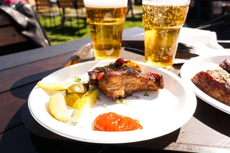 Pork ribs on a tray and light beer on wooden table background. Street food. Festival food on a sunny dayの写真素材