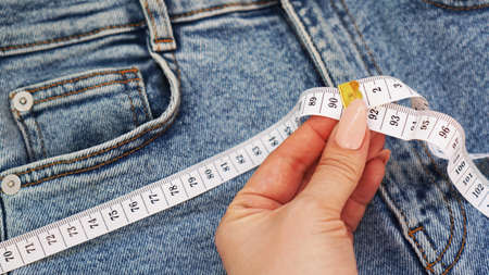 A female hand holds a measuring tape on a denim background. Jeans concept or weight lossの写真素材