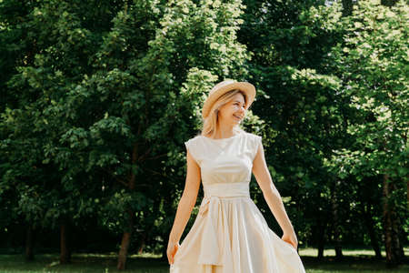 Beautiful young woman in a straw hat and white dress in a green park or forest on a summer dayの写真素材