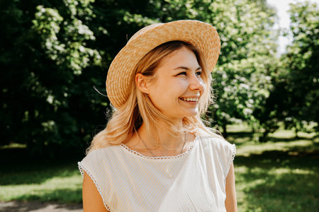 Beautiful young woman in a straw hat and white dress in a green park or forest on a summer day