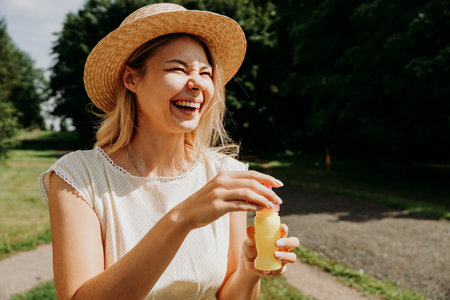 Close portrait of blonde woman in straw hat. She laughs and holds a bottle of soap bubbles. The...