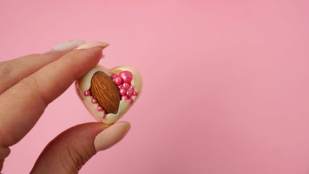 Hand holds white chocolate candies with almonds. Heart shaped sweets. Handmade sweets on a pink...