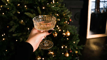 Hand holding stylish vintage wine glass on background of beautiful christmas tree lights. Merry christmas and happy new year concept. Happy holidaysの写真素材