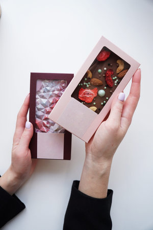 Female hands hold two chocolate bars with a unique design, dried fruits, nuts and decor. Homemade...