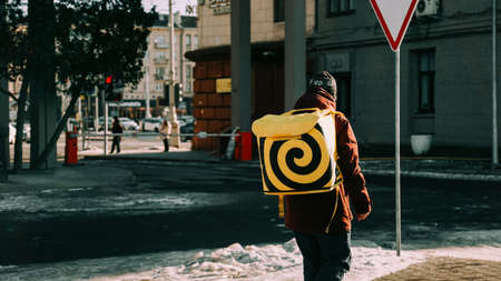 February 2022 - Minsk, Belarus. Deliveryboy walking with yellow and black thermal bag. Man of delivery service in hurry to deliver an orderのeditorial素材