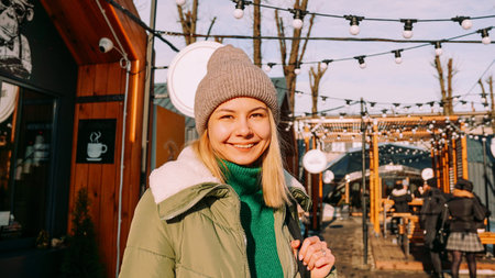 Young blonde at the European street food fair. She is happy and smiling on a sunny winter day....