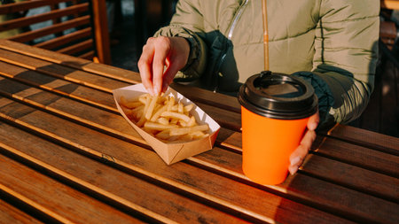 Woman eating tasty french fries and drinking tea or coffee in outdoor cafe. Woman at an urban...