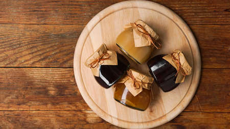 Four glass jars with different kinds of jam on a round cutting board on wooden table. Homemade jam. Top view, space for text. Fruit confitureの写真素材