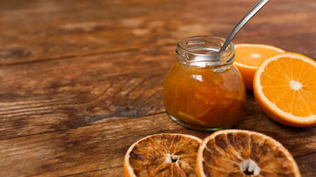 Jar of orange jam, dry oranges on wooden background from top view. Homemade orange marmalade, confiture in thick syrup.の写真素材