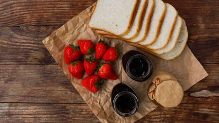 Slices of bread and delicious strawberry jam jar and fresh berries on wooden table. Ingredients for making toast for a delicious breakfast.の写真素材