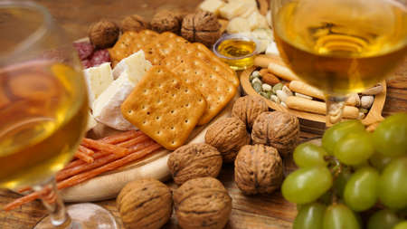 Snacks for wine. Cheese and meat plate. Sausages, cheese, nuts, grapes, crackers on wooden background. Two glasses of white wine.の写真素材