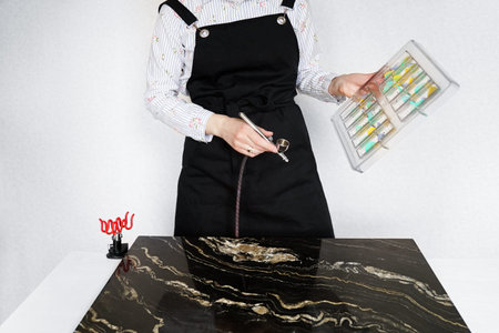 Close-up of the hands of a female pastry chef who sprays food paint with a pastry airbrush in the...