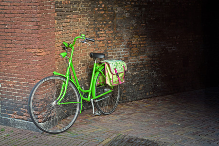 Traditional dutch green bicycle with cycle bag parked in front of a wallの写真素材