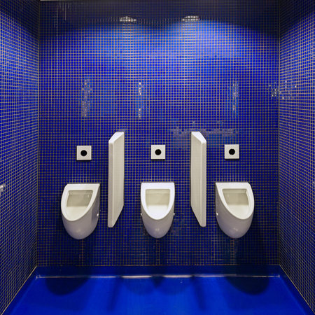 Three white urinals in men public toilet against blue wall.