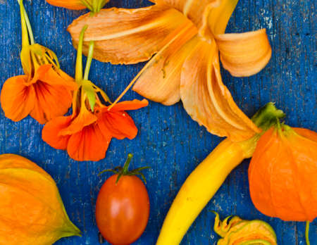Many orange and red flowers and vegetables are messed up on an old blue wooden background and make a beautiful decorationの写真素材
