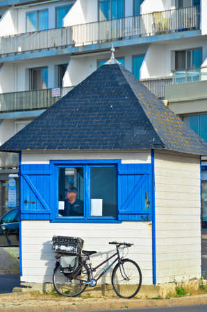 A small house with blue shutters and a bicycle at the front wall of a large houseの写真素材