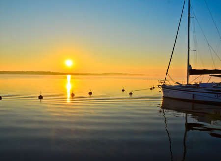 A silhouette of a boat in front of some buoys in calm water in golden evening light.の写真素材