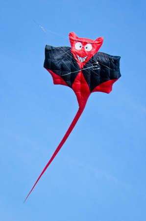 A beautiful, colorful stunt kite, in the blue sky, high in the wind in the form of devilの写真素材
