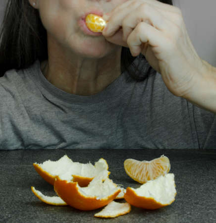 A woman puts on a slice of orange tangerine into her mouth, laying on the table in front of herの写真素材