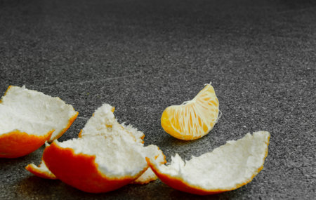 An orange light tangerine on a table, the paring is peeled and a slice of lays on the table