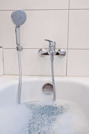 A bathtub in a bathroom filled with warm water and foamの写真素材
