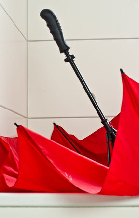 A large red bright umbrella in a white bathtub in a white bathroom for dryingの写真素材