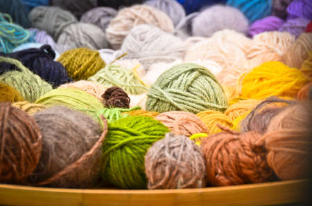 Close up picture of many colorful and vibrant balls, ravels of wool, laying in a large wooden bowl standing on the ground of green grassの写真素材