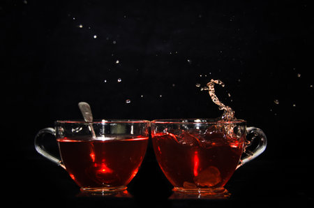 A piece of rock sugar is splashing into one of two glass cups of tea in front of a black backgroundの写真素材