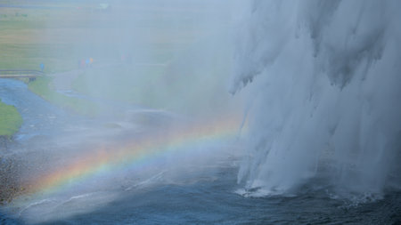 The waterfall of Seljalandsfoss in Iceland from behind the water with a rainbowの写真素材