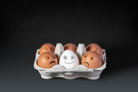 Funny faces and emotions drawn on white and brown eggs with black marker on light background. Carton box with organic chicken eggs on kitchen table closeupの写真素材