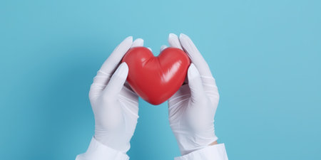 Heart disease prevention concept. Top view photograph of hands in medical gloves holding a heart model on light blue isolated background with copy-spaceの写真素材