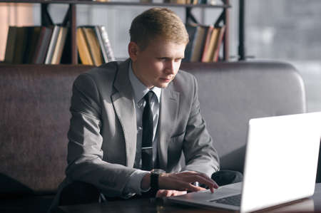 young businessman sitting at desk and working with laptop. looks at the laptop and moving fingers on the trackpadの写真素材