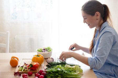 The woman sitting in the kitchen and preparing a fresh vegetable saladの写真素材