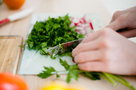 The girl with a knife cuts the dill on the kitchen tableの写真素材