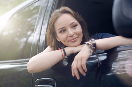 Beautiful girl riding in the car in the passenger seat and leans out the window. She enjoys the road.の写真素材