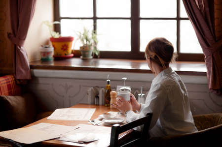 The girl sits in a cafe with a Cup of tea in her hands and looks out the windowの写真素材
