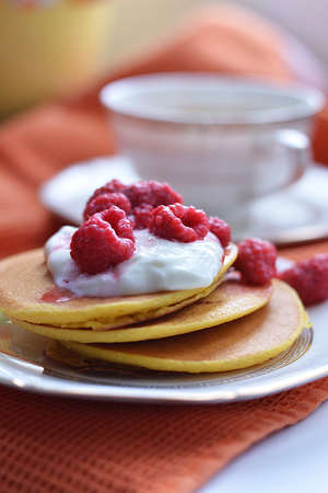 Four corn pancake lie on a white plate with sour cream and raspberry berries, on the background of a Cup of tea.の写真素材