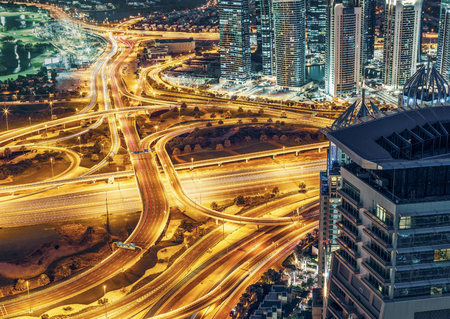 Aerial view of large highway junction in Dubai, UAE, at night with city illuminations and scrapers. Colorful travel and transportation background.の写真素材