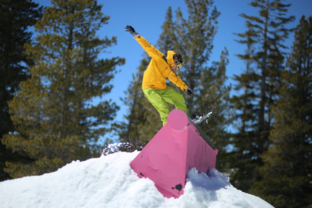 Male jib on a snowboard in a terrain park wearing yellow jacket and green pants