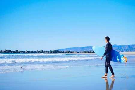 Young surfer caring blue short board on Venice beach, California. Sunny day, good waves and perfect weather.の写真素材